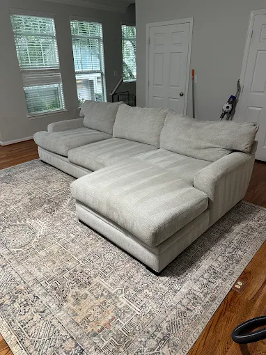 Large gray sectional sofa in bright living room with windows and hardwood floor