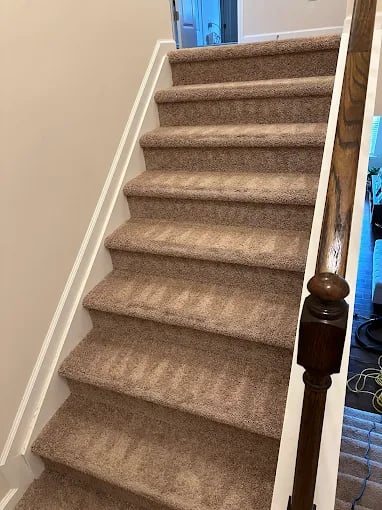 Carpeted stairs with white railing and wooden banister post